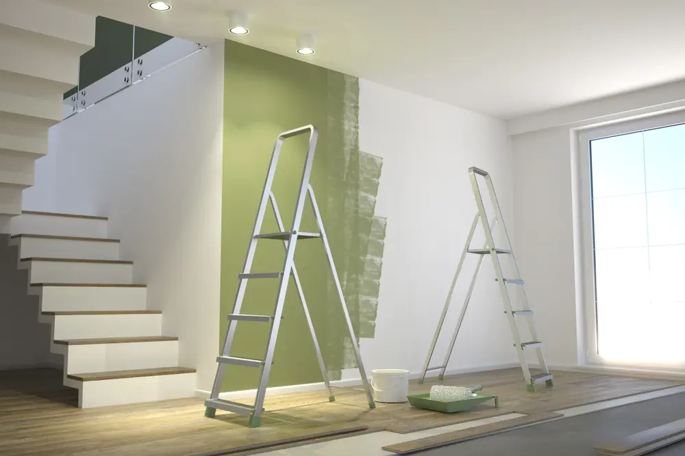 Two ladders and green paint tray beside a stairway show wall makeover in progress, highlighting modern painting options.