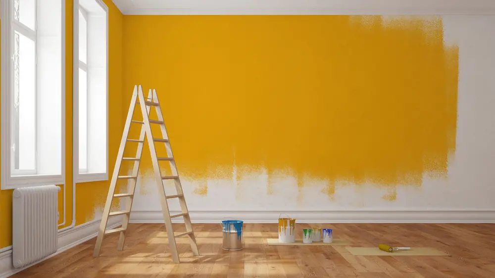 Modern room renovation showing supplies and a ladder to paint interior walls with vibrant yellow color.