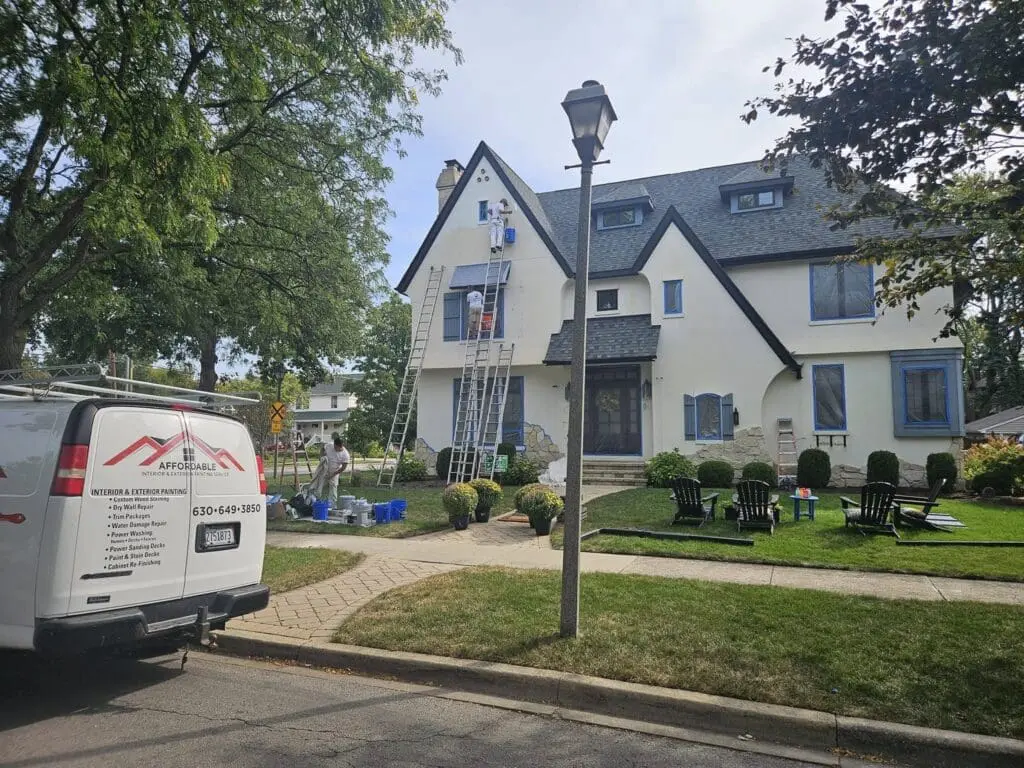 Painting contractor team applying exterior paint to large home in Western Springs, preparing surfaces with proper equipment.