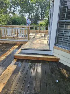 A person applying treatment to a newly installed section of a wooden deck during a restoration project.