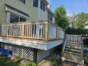 A raised backyard deck with stair access and partially painted railings, undergoing repair and refinishing outside a yellow home.