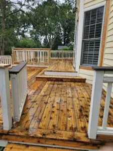 A freshly sanded and cleaned wooden deck with white railings outside a yellow house, ready for staining or sealing.
