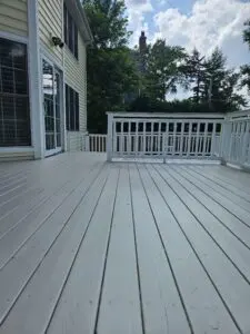 A freshly painted backyard deck with smooth, light-gray boards and white railings outside a yellow two-story home.