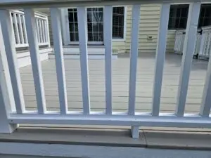 Close-up view through freshly painted white deck railings showing a smooth, light-gray deck surface in front of a yellow house.