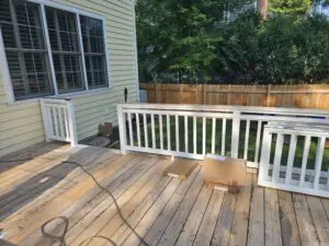 A wooden deck in the process of being stripped, with removed railing sections, exposed boards, and packaging materials laid out.