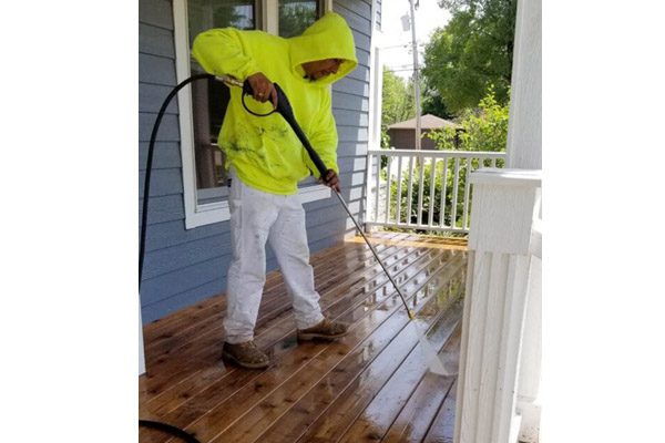 A man in yellow jacket using a hose on porch.