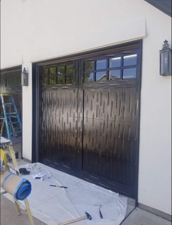 A garage door that is painted black and has two windows.