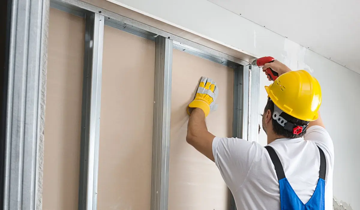 Professional contractor using a drill to replace and repair drywall on a metal frame.