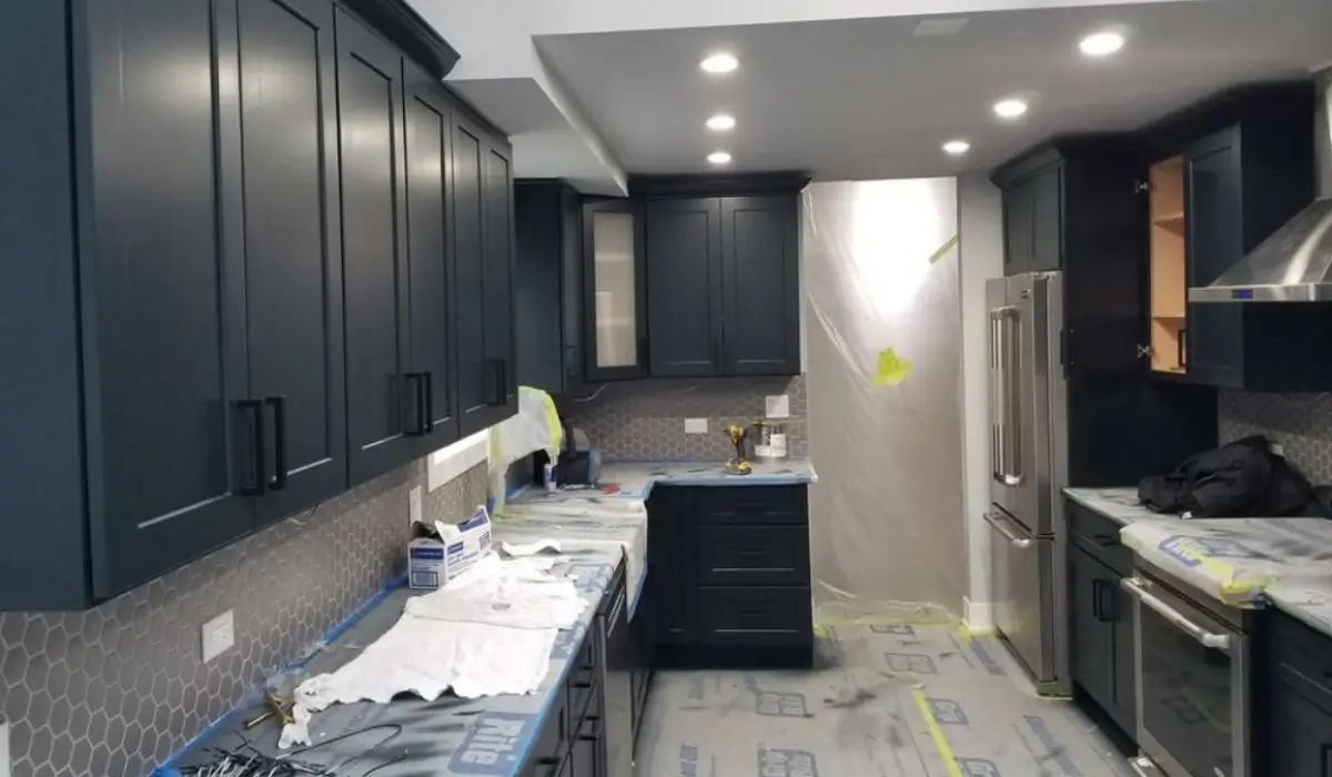 Kitchen cabinets being professionally painted with dark finish, improving kitchen aesthetics and durability during refinishing process.