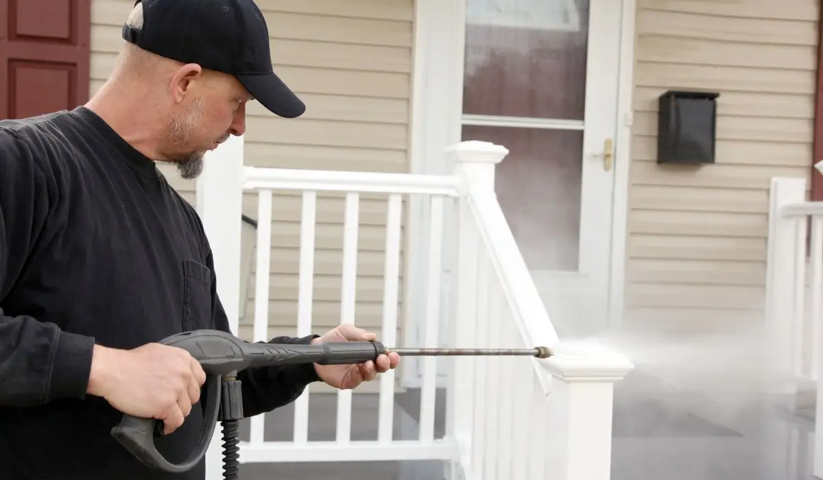 Professional using power wash equipment to clean exterior railing before house painting for optimal surface preparation.