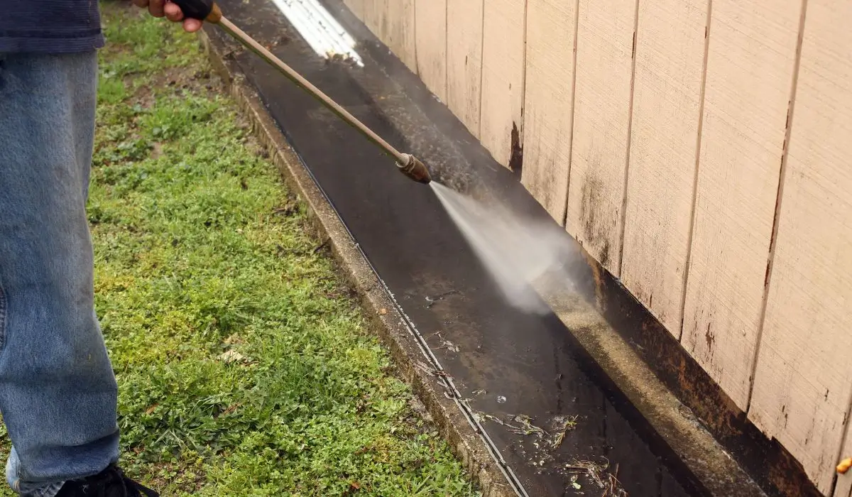 A technician power washing the base of a home to clean mold and grime buildup along the foundation and siding