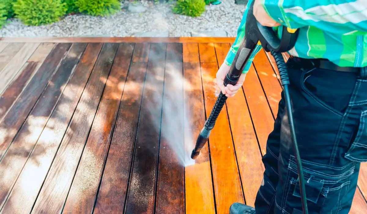 A professional using power washing equipment to clean a dirty wood deck, removing stains and buildup for a refreshed look.