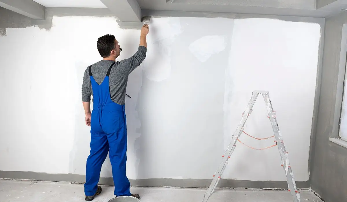 A professional painter in blue overalls uses a brush to repaint your home’s interior walls for a refreshed look.