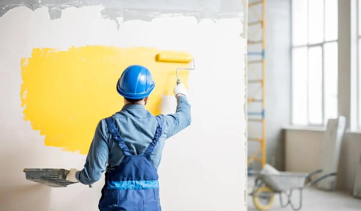 Professional painter applying smooth yellow paint finish on white wall, illustrating ideal paint finish for living spaces.