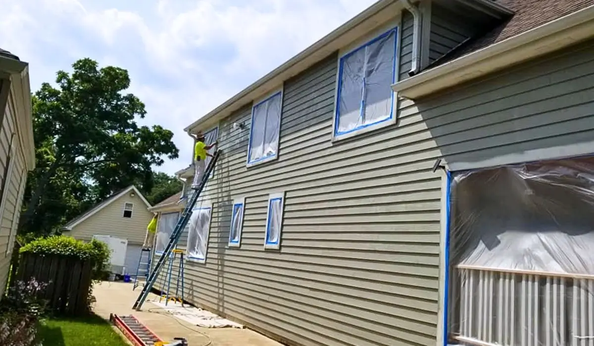 Professional painters preparing house siding with protective masking before applying exterior paint, preventing spring weather-related damage.