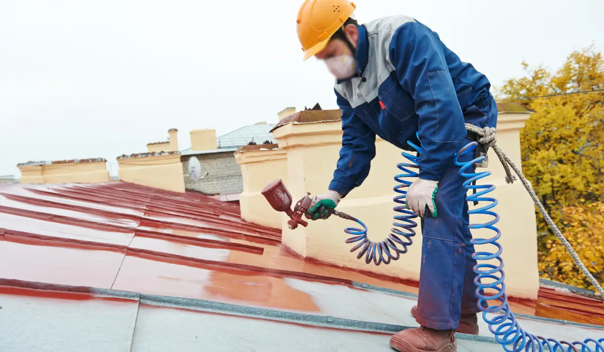 Professional painter applying roof coating with a sprayer on an overcast fall day in Hinsdale, wearing safety gear and cold-weather workwear.