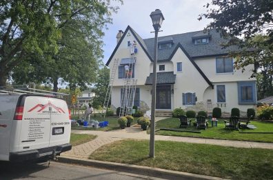 Painting contractor team applying exterior paint to large home in Western Springs, preparing surfaces with proper equipment.